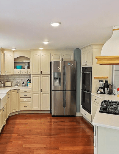 A bright, spacious kitchen with wooden flooring, cream-colored cabinetry, and stainless steel appliances.